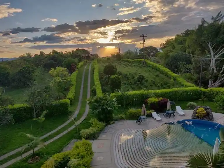 Piscina y jardines exuberantes al atardecer en una finca rural en Alcalá, Valle del Cauca, ideal para alojamiento.