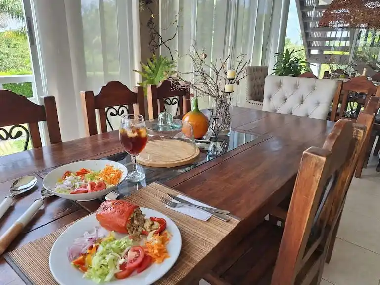 Mesa de comedor de madera con pimientos rellenos y ensaladas en un ambiente luminoso de finca en Alcalá, Valle.