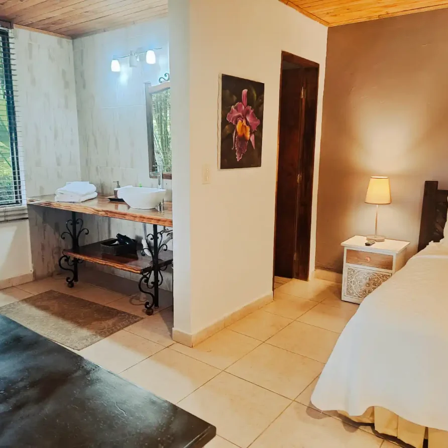 Interior de habitación de hospedaje en Alcalá Valle, con cama, mesita y tocador con lavamanos moderno.