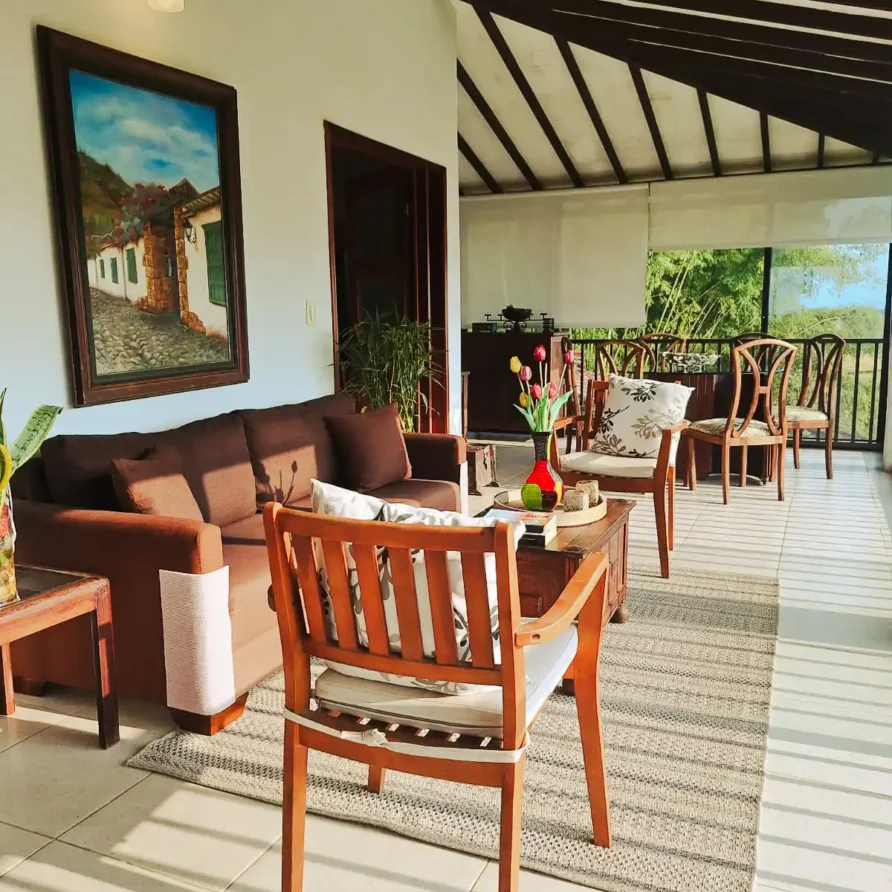 Zona común luminosa de hotel o finca en Alcalá, Valle del Cauca, con asientos cómodos y acceso a terraza con vista verde.