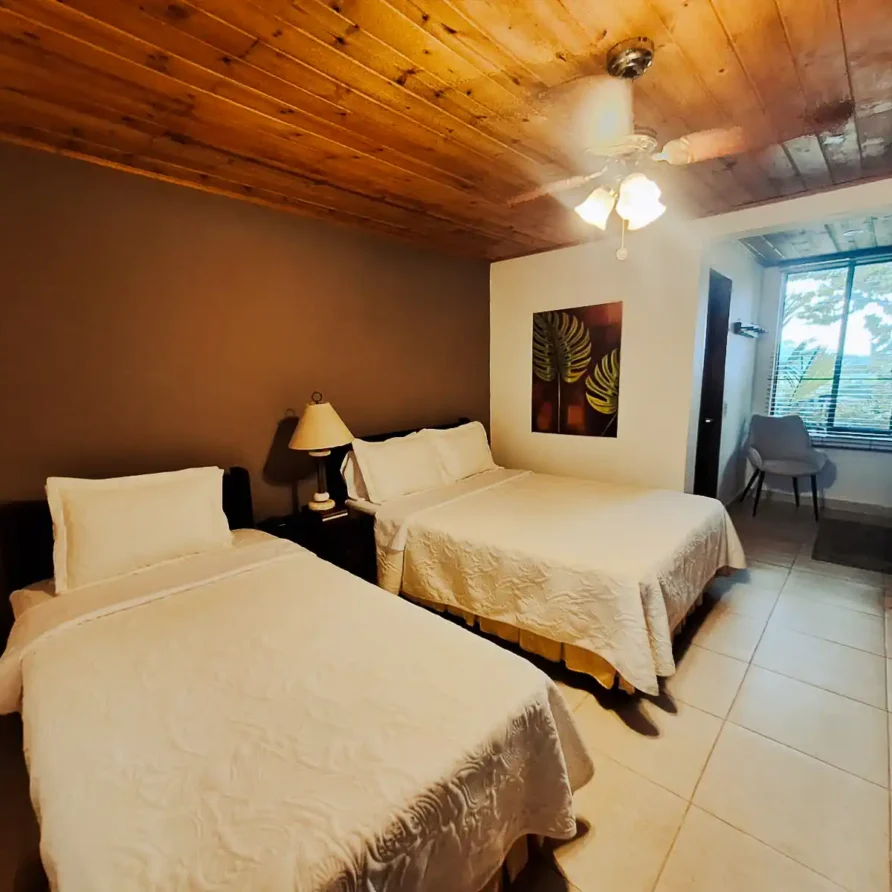 Amplia habitación de hospedaje en Alcalá, Valle del Cauca, con dos camas, mobiliario moderno y vista exterior.