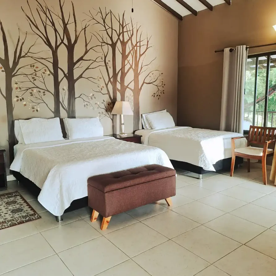 Habitación suite de hotel en Alcalá Valle con dos camas, mural de árboles, ventilador de techo y vista a la naturaleza.