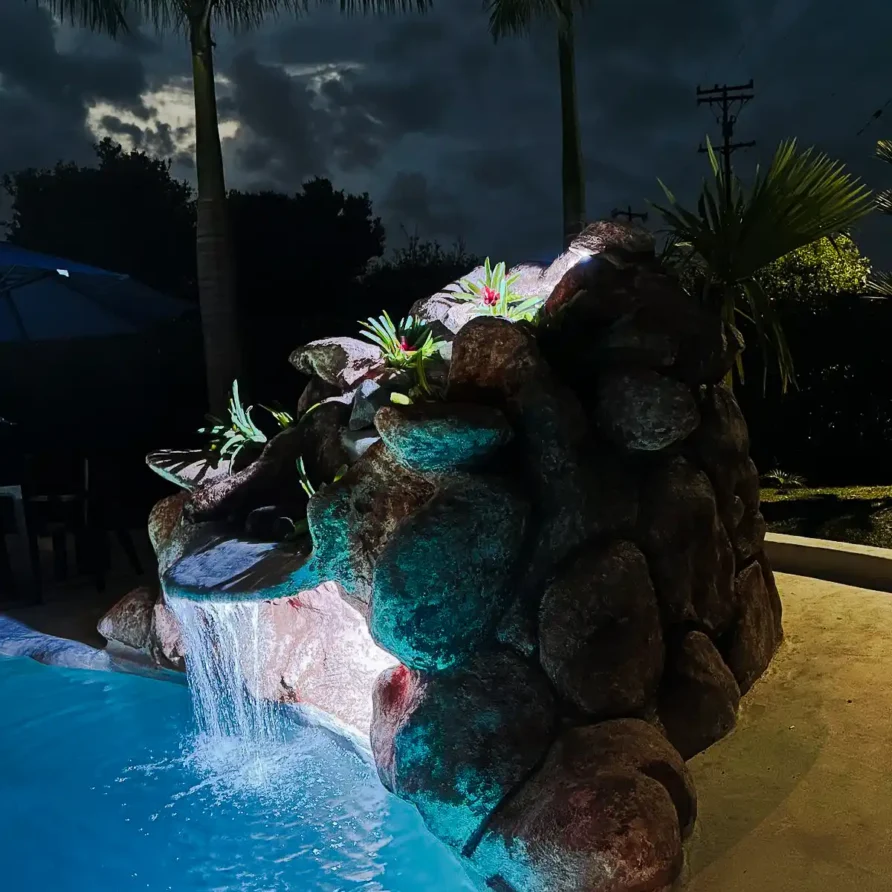 Piscina iluminada con cascada de rocas en finca hotel Alcalá Valle del Cauca, ideal para relajación nocturna.