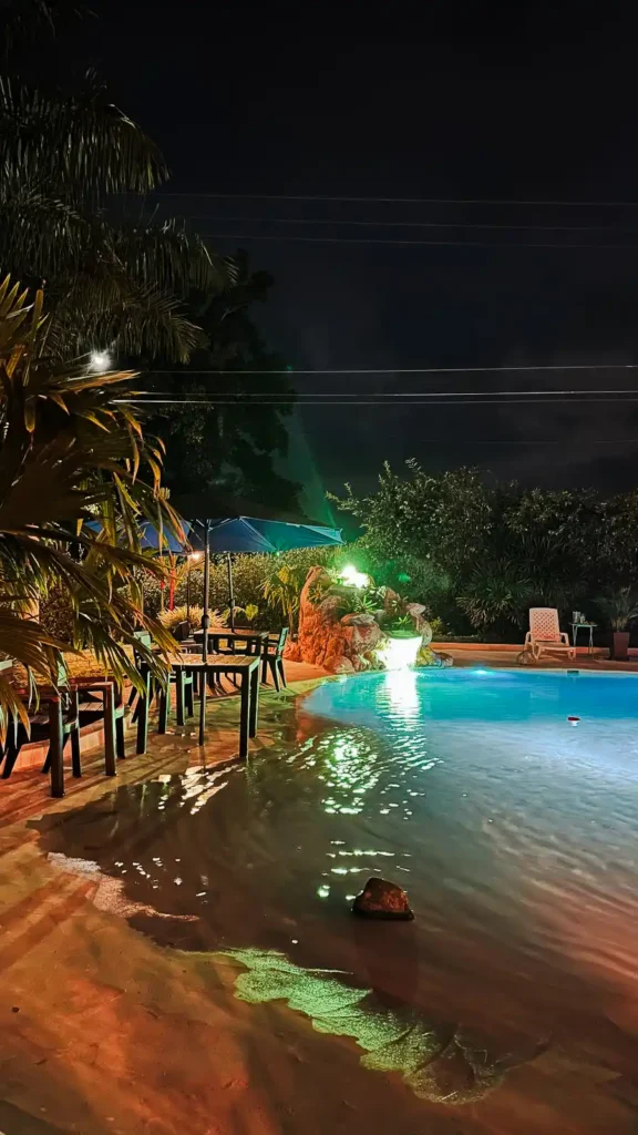 Piscina iluminada de noche en finca hotel en Alcalá Valle del Cauca, con mesas y palmeras, ideal para alojamiento.