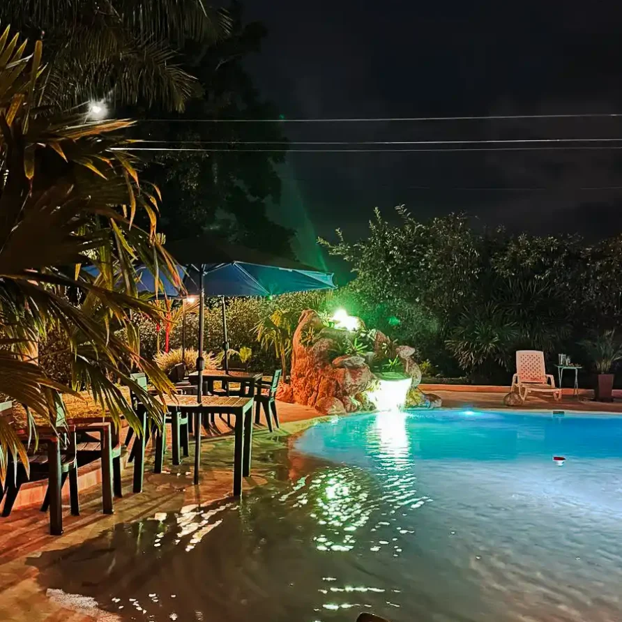 Piscina iluminada de noche en finca hotel en Alcalá Valle del Cauca, con mesas y palmeras, ideal para alojamiento.