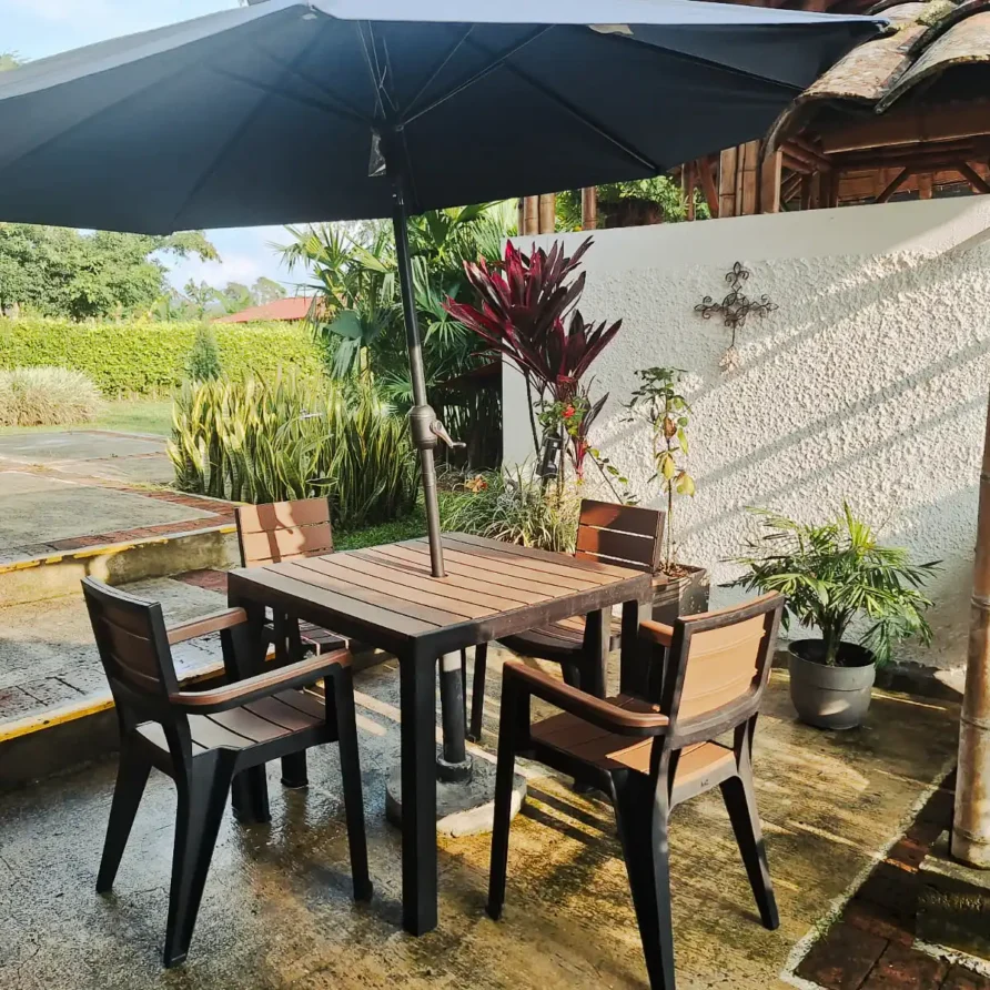 Área de patio sombreada con mesa y sillas de jardín, rodeada de plantas, ideal para el hospedaje en Alcalá.